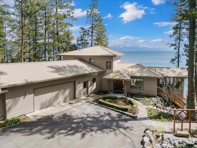 prairie-style home featuring an attached garage, a water view, metal roof, and aphalt driveway