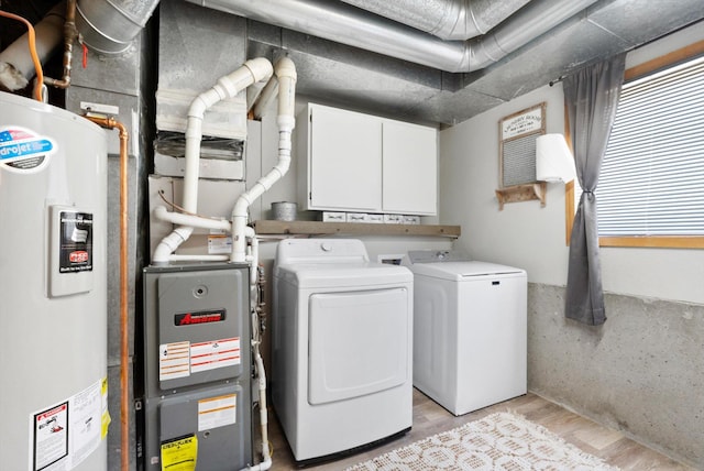 clothes washing area with electric water heater, washer and clothes dryer, and light wood-type flooring