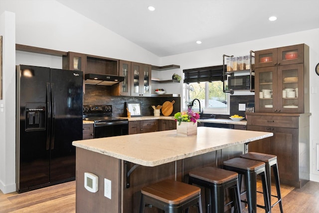 kitchen with under cabinet range hood, decorative backsplash, black appliances, and light wood-style floors