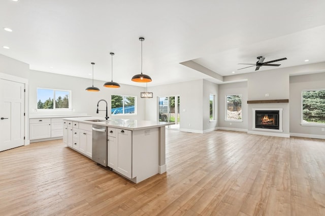 kitchen with stainless steel dishwasher, a wealth of natural light, light wood finished floors, a sink, and light countertops
