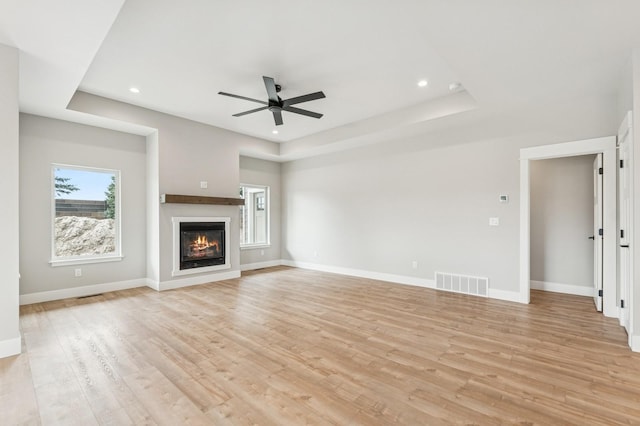 unfurnished living room with light wood-type flooring, visible vents, a ceiling fan, and a glass covered fireplace