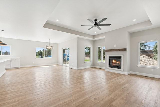 unfurnished living room featuring plenty of natural light, ceiling fan with notable chandelier, a glass covered fireplace, and light wood-style floors