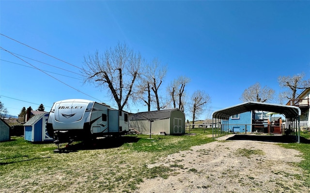 view of yard with a storage unit, fence, a detached carport, an outbuilding, and driveway
