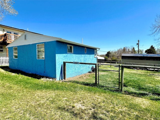 view of side of property with a lawn, stucco siding, fence, and a gate