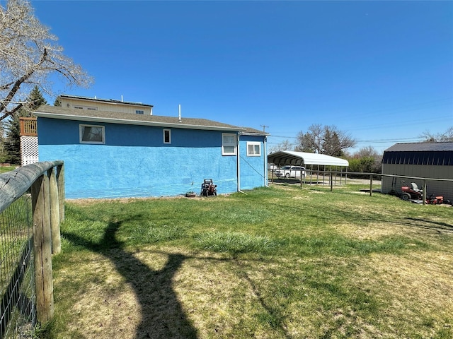 back of property featuring a detached carport, fence, stucco siding, and a yard