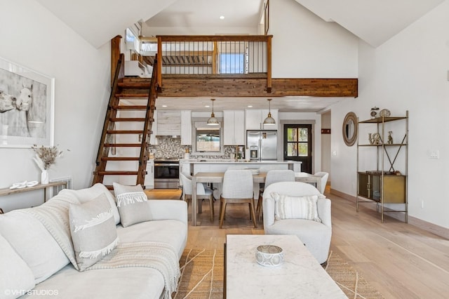 living area featuring stairway, light wood-style flooring, baseboards, and high vaulted ceiling