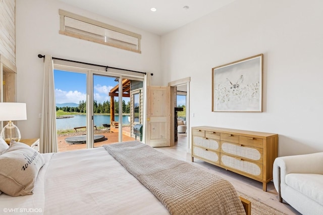 bedroom with a water view, access to outside, light wood-style flooring, and a high ceiling