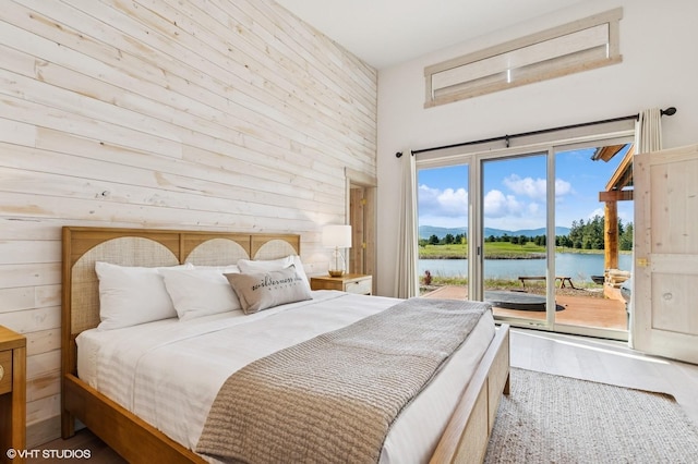 bedroom featuring a water view, access to outside, a high ceiling, and wood finished floors