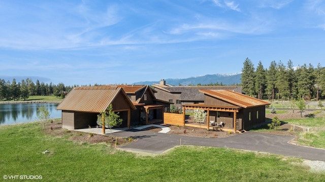 view of front facade with a water and mountain view, a front lawn, and a chimney