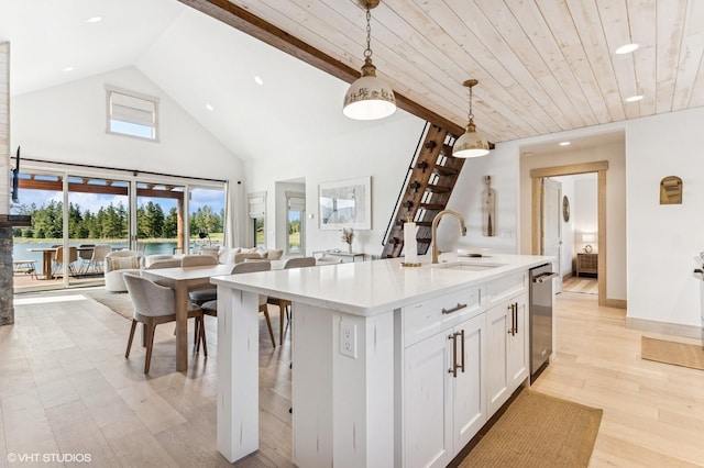 kitchen with hanging light fixtures, a sink, open floor plan, white cabinets, and stainless steel dishwasher