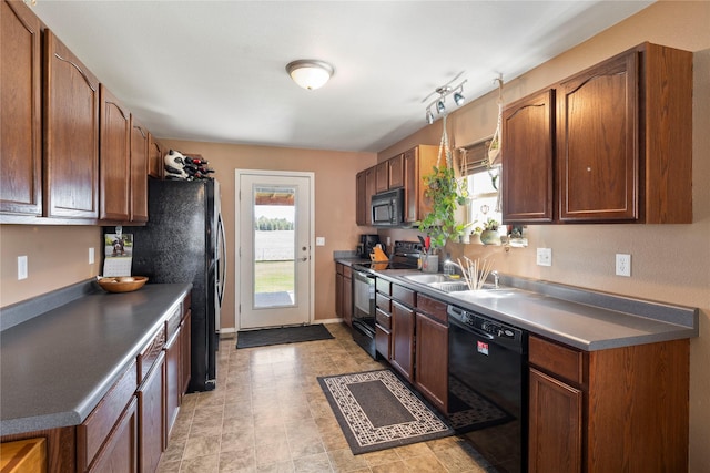 kitchen with a sink, brown cabinetry, black appliances, baseboards, and dark countertops