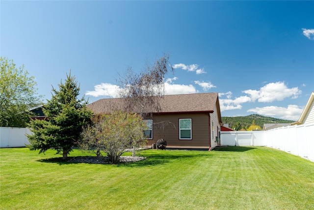back of property featuring a lawn, roof with shingles, and a fenced backyard