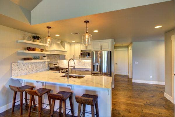 kitchen with baseboards, custom exhaust hood, a sink, a peninsula, and stainless steel appliances