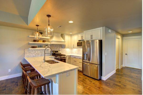 kitchen with a sink, a peninsula, custom exhaust hood, baseboards, and appliances with stainless steel finishes