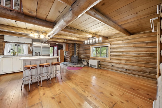 1441 Bonanza Dr, Sula, MT 59871 - kitchen featuring stainless steel refrigerator with ice dispenser, a wood stove, rustic walls, wood ceiling with exposed beams, and a sink