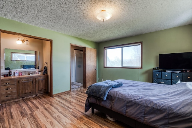 bedroom featuring a textured ceiling, ensuite bathroom, wood finished floors, and a sink