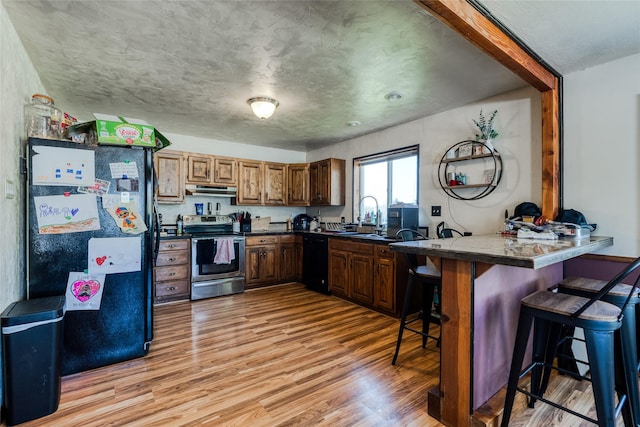 kitchen with under cabinet range hood, a breakfast bar, light wood finished floors, a peninsula, and black appliances
