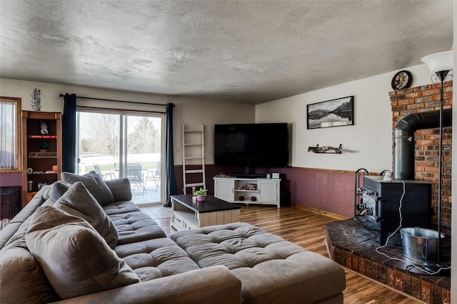 living area featuring a wood stove, a textured ceiling, a wainscoted wall, and wood finished floors