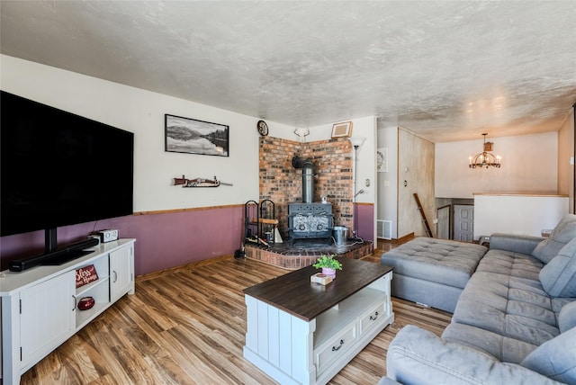 living room featuring a chandelier, light wood finished floors, a wood stove, and visible vents