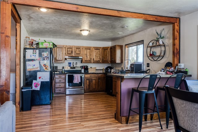 kitchen featuring a peninsula, black appliances, under cabinet range hood, dark countertops, and light wood-style floors