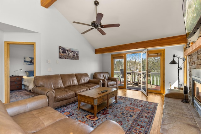 living room featuring beam ceiling, wood finished floors, high vaulted ceiling, ceiling fan, and a stone fireplace
