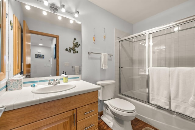 full bath with toilet, bath / shower combo with glass door, vanity, and wood finished floors