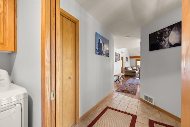 hall featuring light tile patterned floors, visible vents, baseboards, and washer / clothes dryer