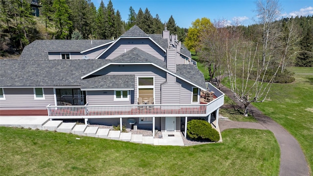 back of house featuring roof with shingles, a deck, a yard, a patio, and a chimney