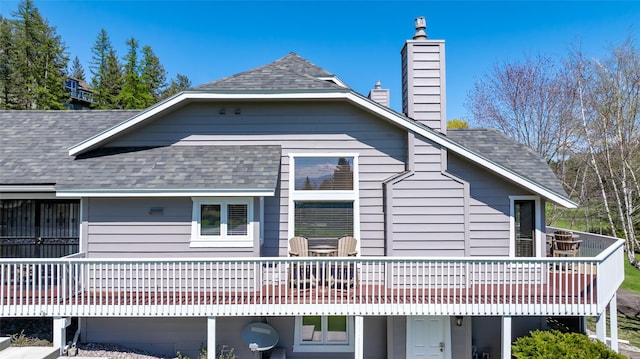 view of side of home featuring roof with shingles, a wooden deck, and a chimney