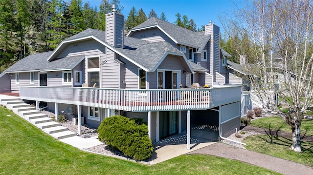 back of property with a chimney, a yard, a patio area, a shingled roof, and a deck