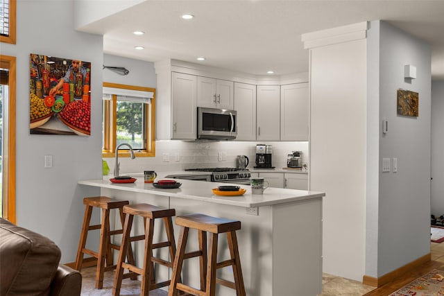 kitchen featuring a peninsula, a kitchen breakfast bar, light countertops, tasteful backsplash, and appliances with stainless steel finishes