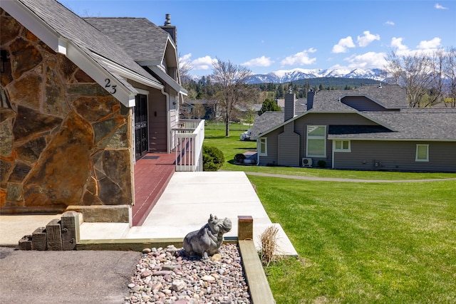 view of side of property featuring a mountain view, a patio, a chimney, a lawn, and a shingled roof