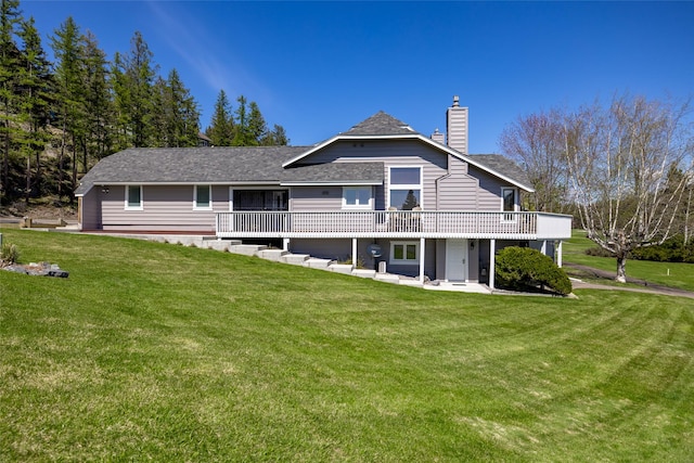 rear view of house featuring a yard, a deck, a shingled roof, and a chimney