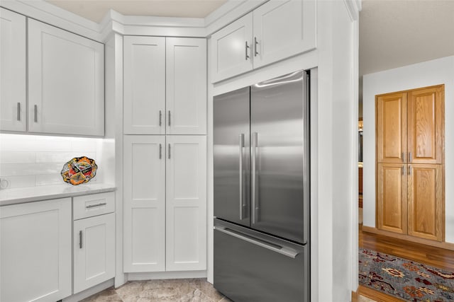 kitchen with white cabinetry, stainless steel built in refrigerator, and backsplash