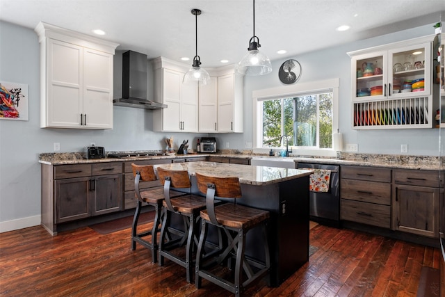 kitchen with stainless steel appliances, wall chimney exhaust hood, dark wood-style floors, a kitchen bar, and white cabinetry