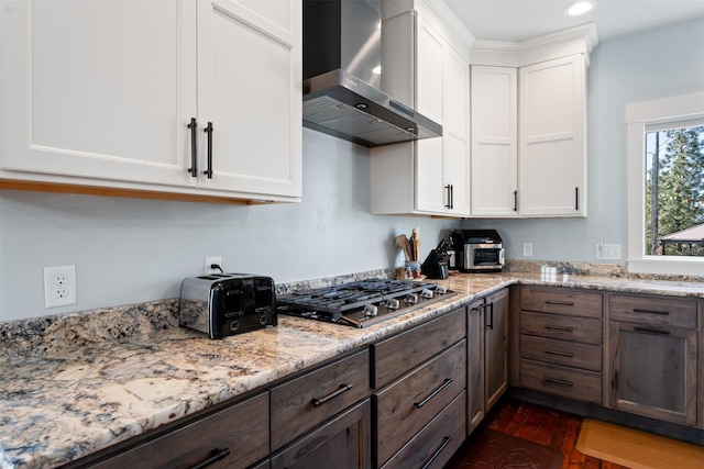 kitchen with wall chimney exhaust hood, stainless steel gas cooktop, white cabinets, light stone counters, and dark wood-type flooring
