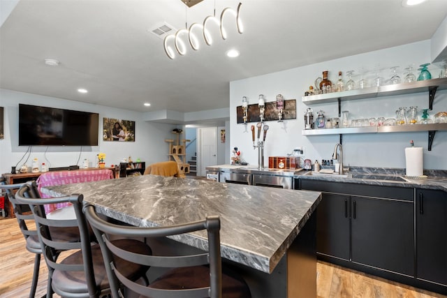 kitchen featuring dark cabinetry, light wood-style flooring, a kitchen bar, recessed lighting, and a sink