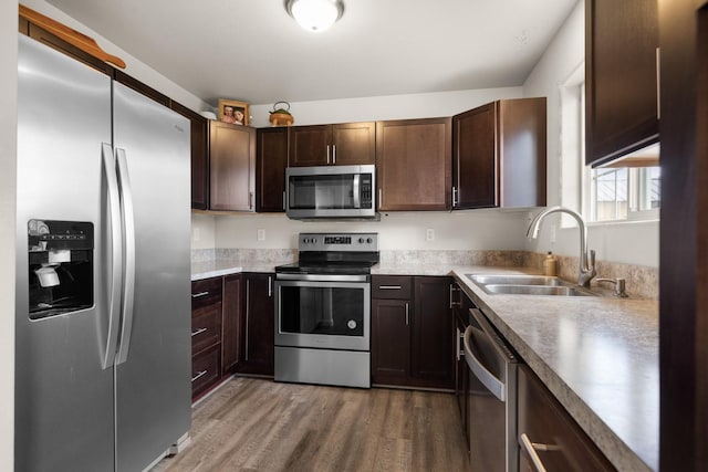 kitchen featuring light wood-style floors, appliances with stainless steel finishes, dark brown cabinetry, and a sink