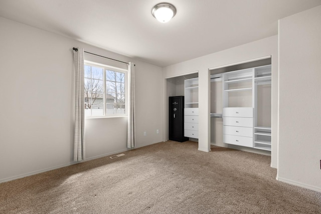 unfurnished bedroom with baseboards, multiple closets, visible vents, and carpet floors