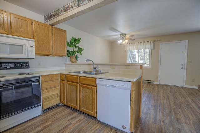 kitchen with a sink, a peninsula, white appliances, and wood finished floors