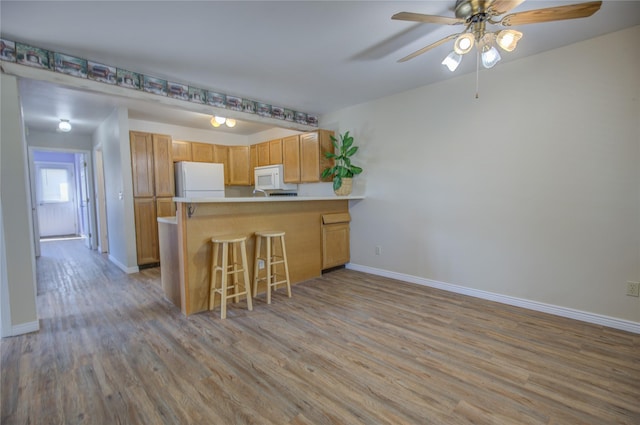 kitchen featuring a peninsula, white appliances, ceiling fan, baseboards, and light wood-style floors