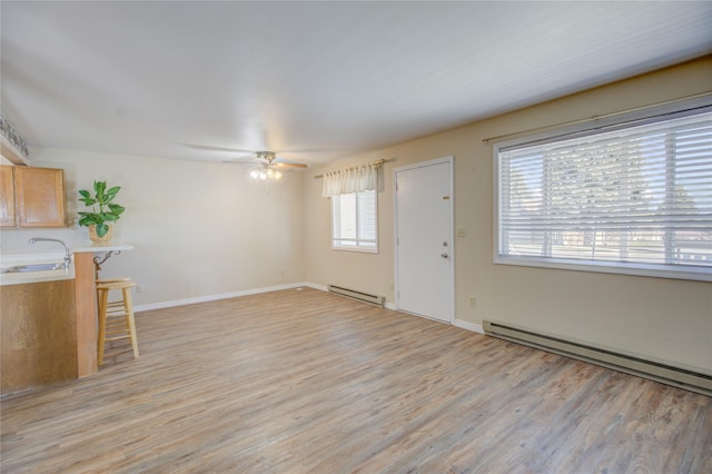 unfurnished living room featuring a sink, light wood finished floors, ceiling fan, and a baseboard heating unit