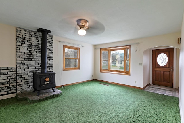 unfurnished living room with a wood stove, visible vents, carpet floors, a ceiling fan, and baseboards