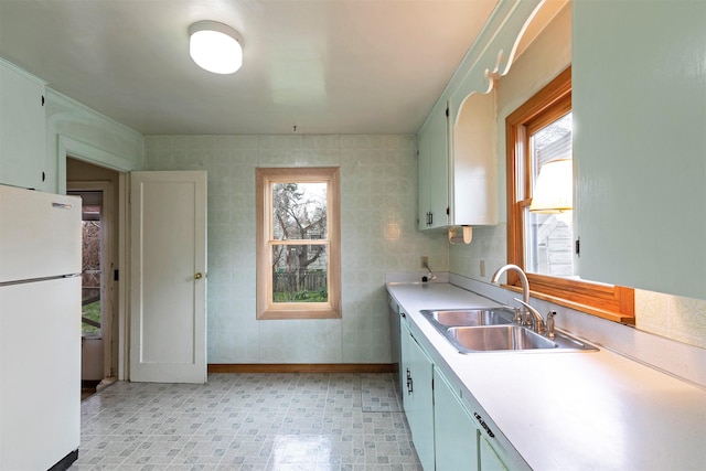 kitchen featuring freestanding refrigerator, baseboards, light countertops, and a sink