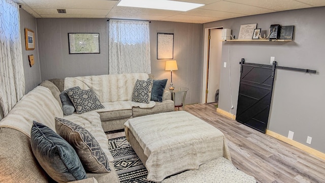 living room featuring wood finished floors, a paneled ceiling, visible vents, a barn door, and baseboards