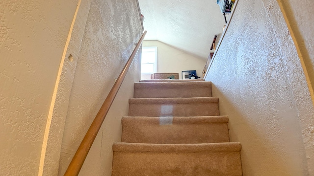 stairway with lofted ceiling and a textured wall