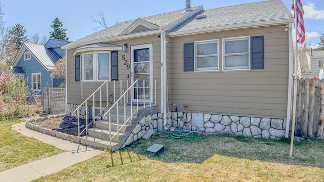 view of front facade featuring a front yard, a shingled roof, and fence