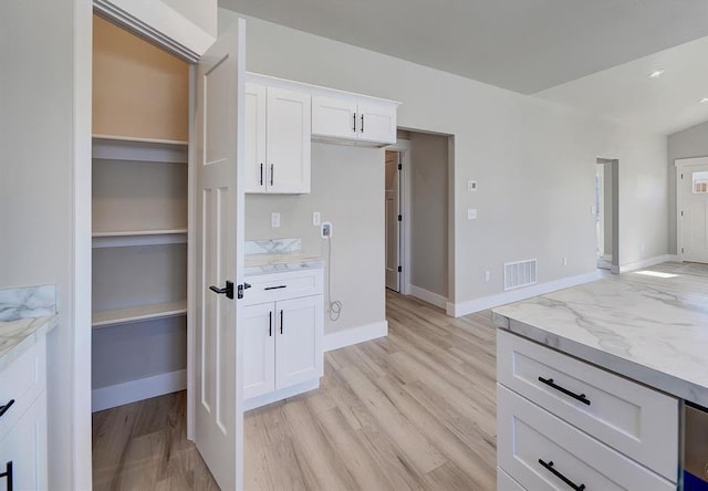 kitchen featuring light stone counters, visible vents, light wood-style flooring, white cabinetry, and baseboards