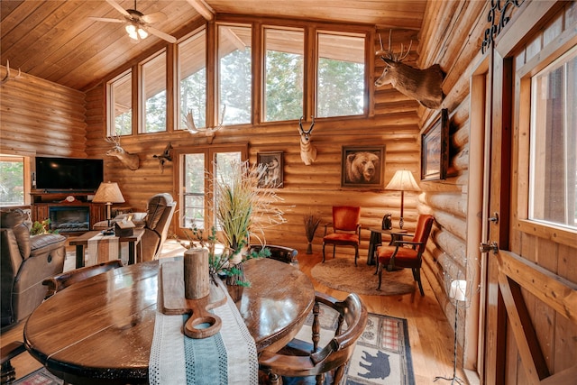 dining room featuring high vaulted ceiling, ceiling fan, a glass covered fireplace, rustic walls, and hardwood / wood-style flooring