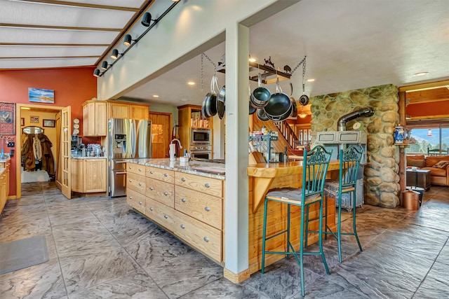 kitchen with appliances with stainless steel finishes, light marble finish flooring, vaulted ceiling, light brown cabinetry, and light stone counters